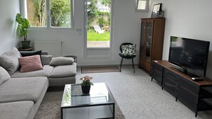 Ett vardagsrum med en soffa, ett soffbord i glas med en växt, en tv och ett skåp.