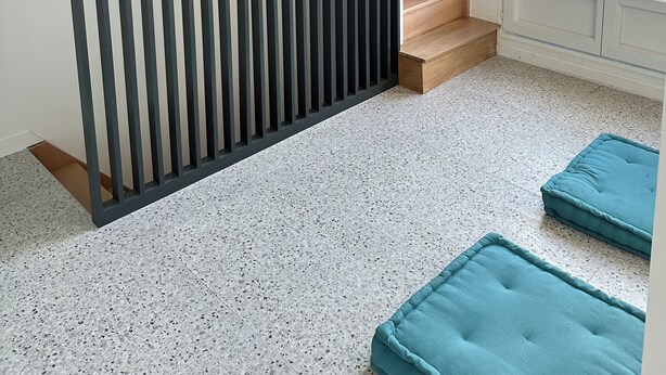 Ett rum med modern design, med en skjutdörr med vertikala lameller, en trappa som leder ut till ett utomhusområde och två blå sittgrupper med bekväma kuddar.