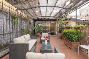Une terrasse extérieure avec des meubles en osier, une table en verre et des plantes en pot.