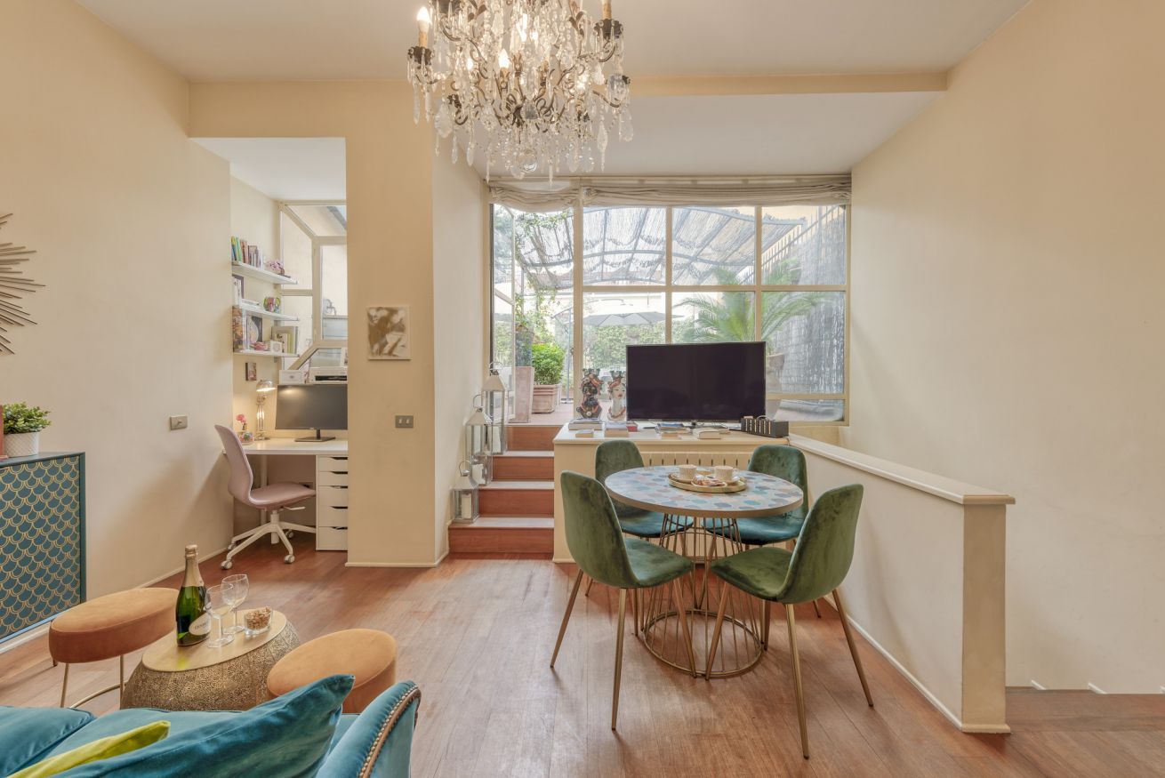 A modern living space with a dining area, a workspace, and a large window with a view of greenery.