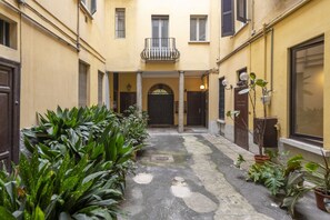 Un cortile con un arco centrale, piante in vaso e un piccolo balcone.