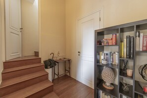Un escalier menant à une porte, une petite table avec un sac à main, et une bibliothèque remplie de livres et d’objets décoratifs.