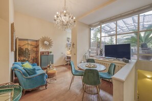 Un salon avec un canapé bleu, un lustre, une table ronde et un téléviseur.