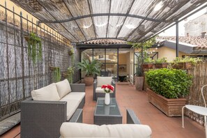 An outdoor patio with wicker furniture, a glass table, and potted plants. - BnButler - Pontaccio, 4 with terrace (Milano)