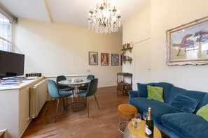 Un soggiorno con un divano blu, un lampadario, un tavolo da pranzo con sedie e un televisore su un mobile.