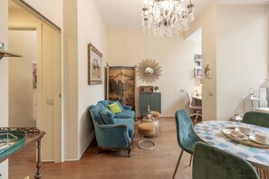 Un salon comprenant un canapé, des fauteuils, une table à manger avec un plateau, un lustre et un miroir décoratif.