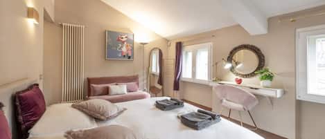 Un dormitorio con cama, escritorio, silla, radiador, espejo y ventana.