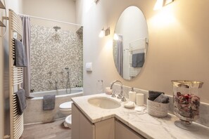 Une salle de bain moderne équipée d’une baignoire, de toilettes et d’un lavabo, avec une zone de douche carrelée et un grand miroir.