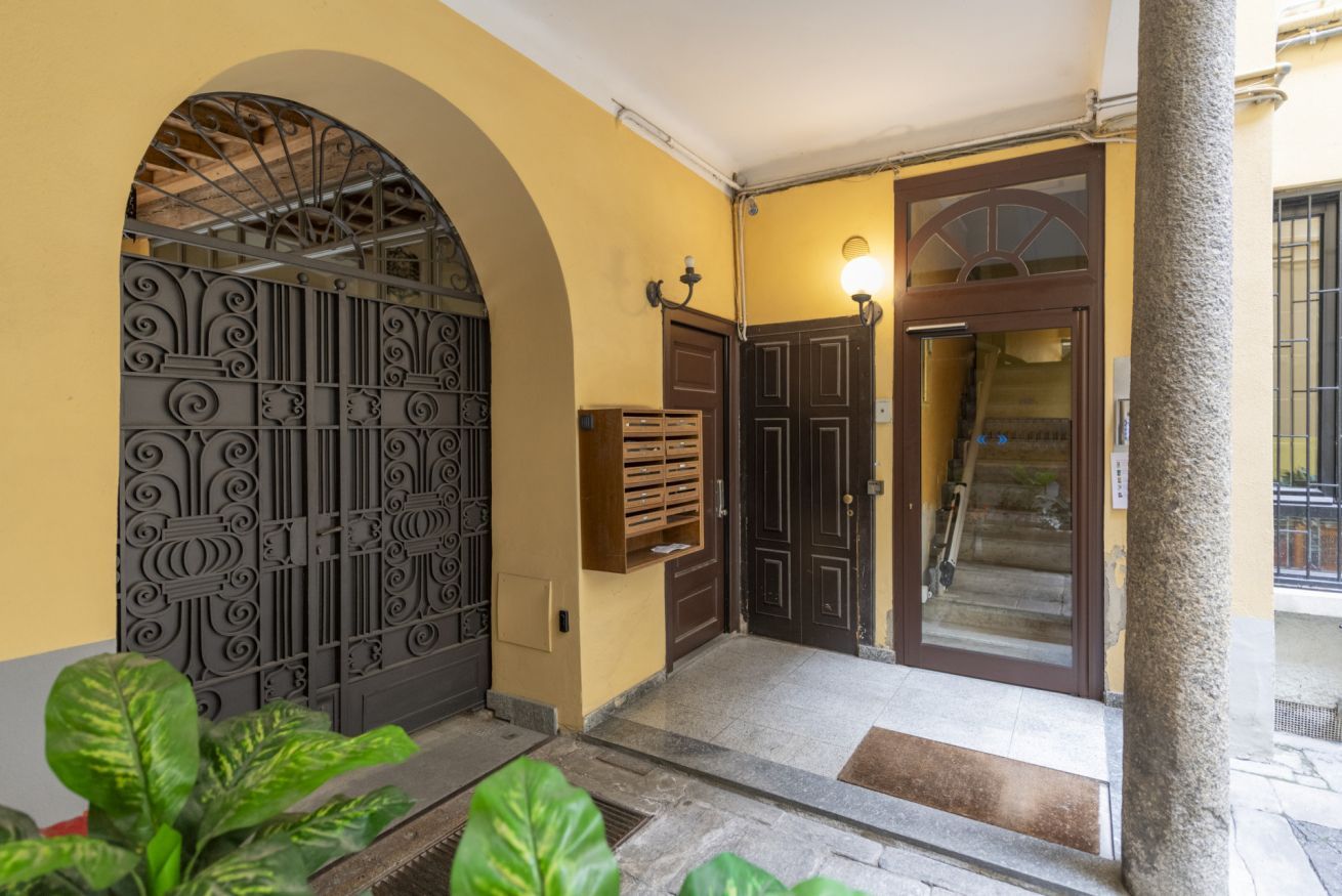Entrada de um edifício com portão de metal, porta de madeira e escadaria que dá acesso ao interior.