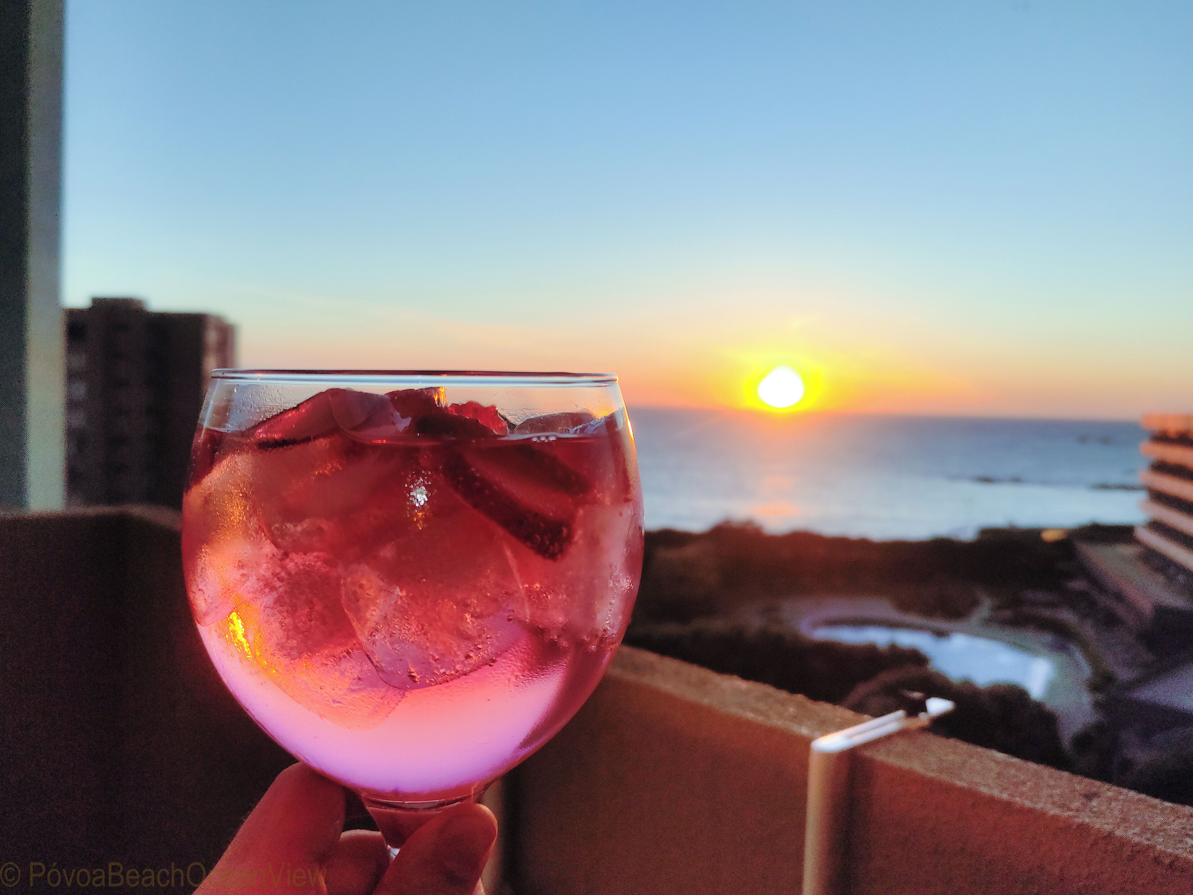 Solnedgangsudsigte fra en balkon med et glas rød drik.