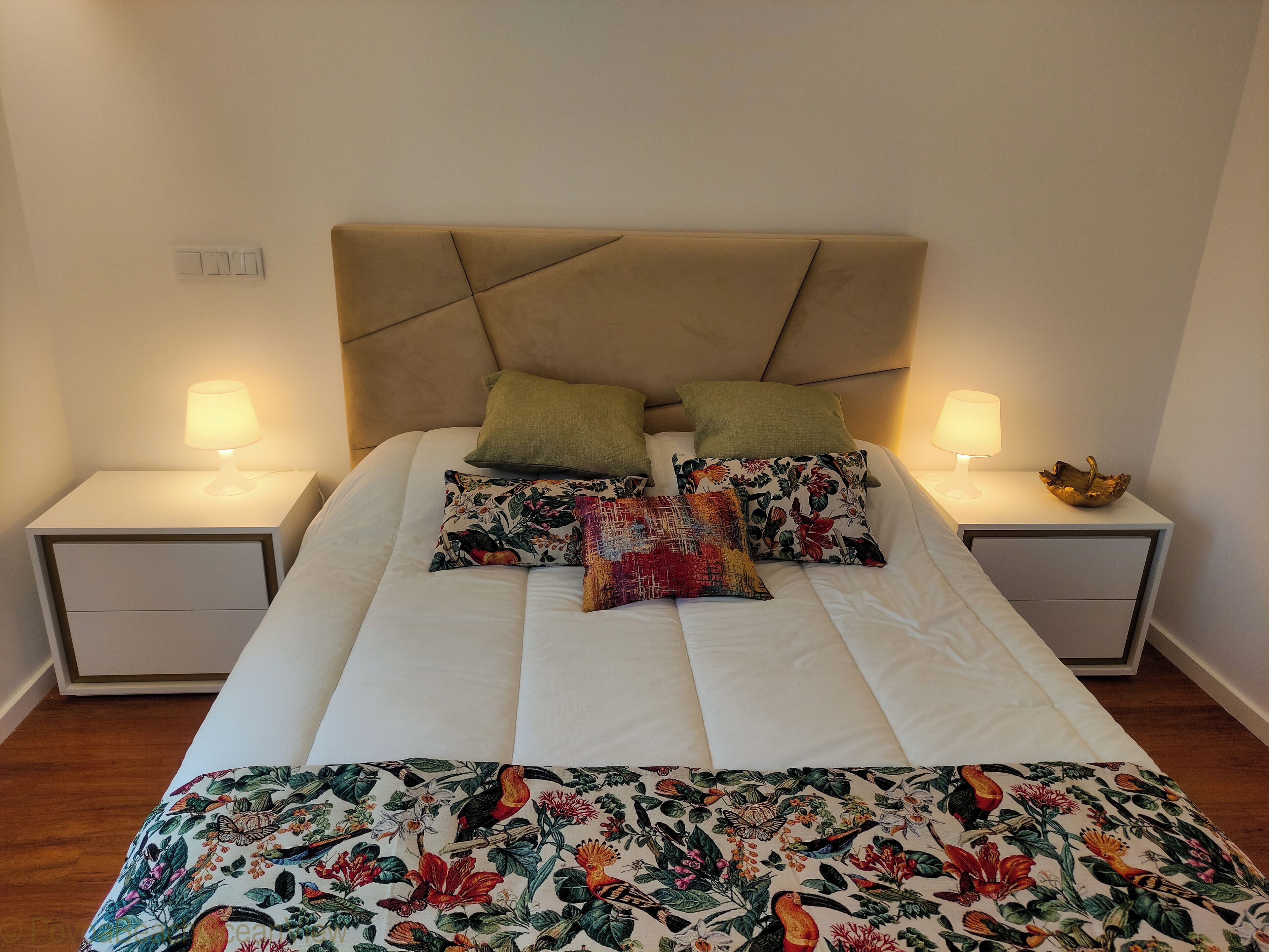 Un lit avec une tête de lit de couleur beige, deux tables de chevet avec des lampes et une literie à motifs floraux.