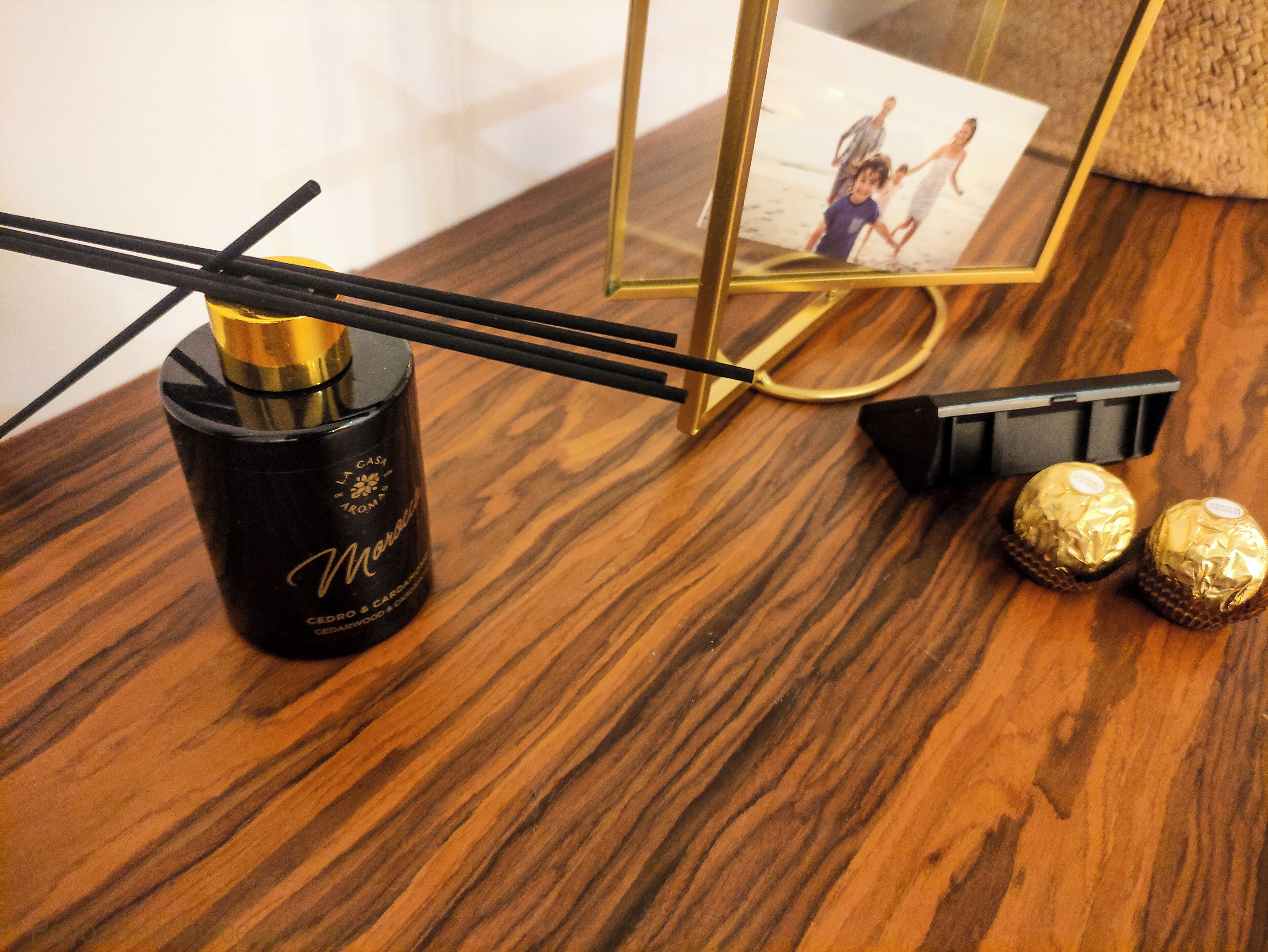 Une table en bois, sur laquelle se trouvent un récipient cylindrique noir, deux chocolats emballés et une paire de baguettes.