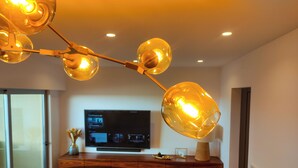 Un salon moderne avec un meuble de rangement en bois pour l’équipement audiovisuel, un téléviseur à écran plat et un lustre original.