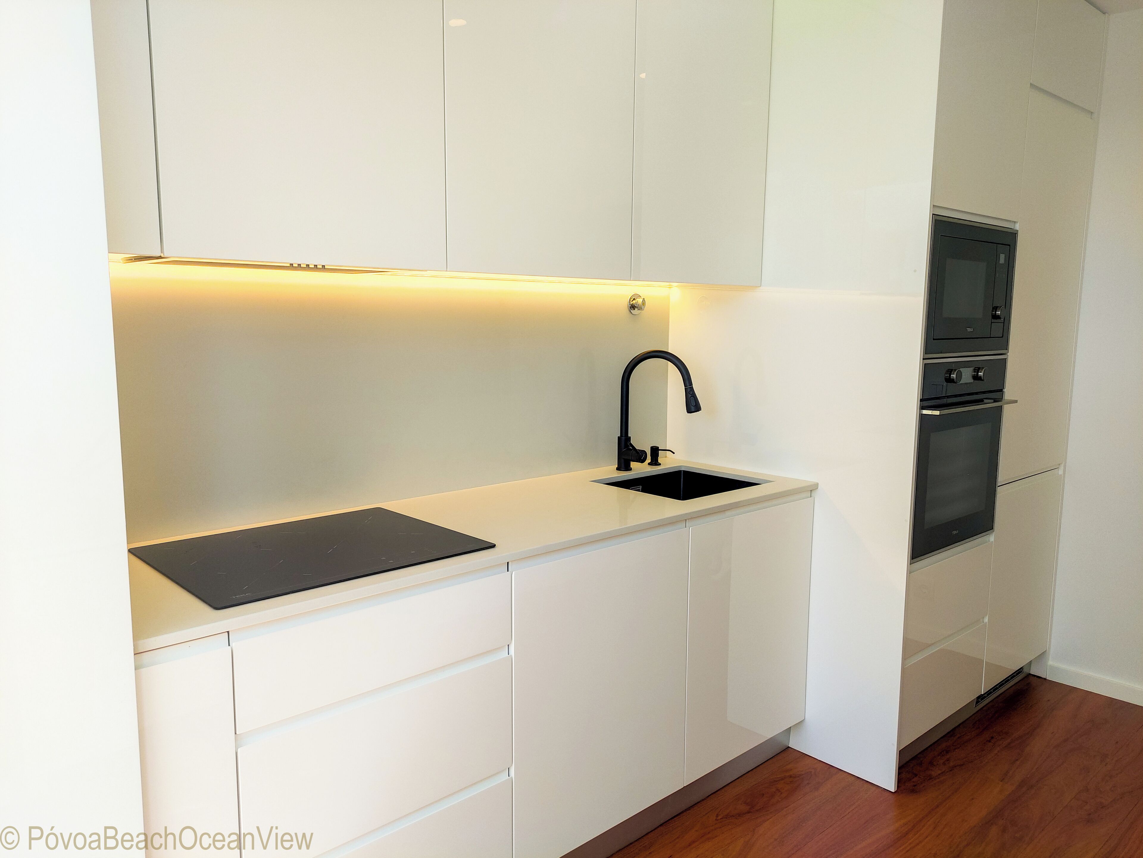 A modern kitchen with white cabinetry, a black sink, and a built-in oven.