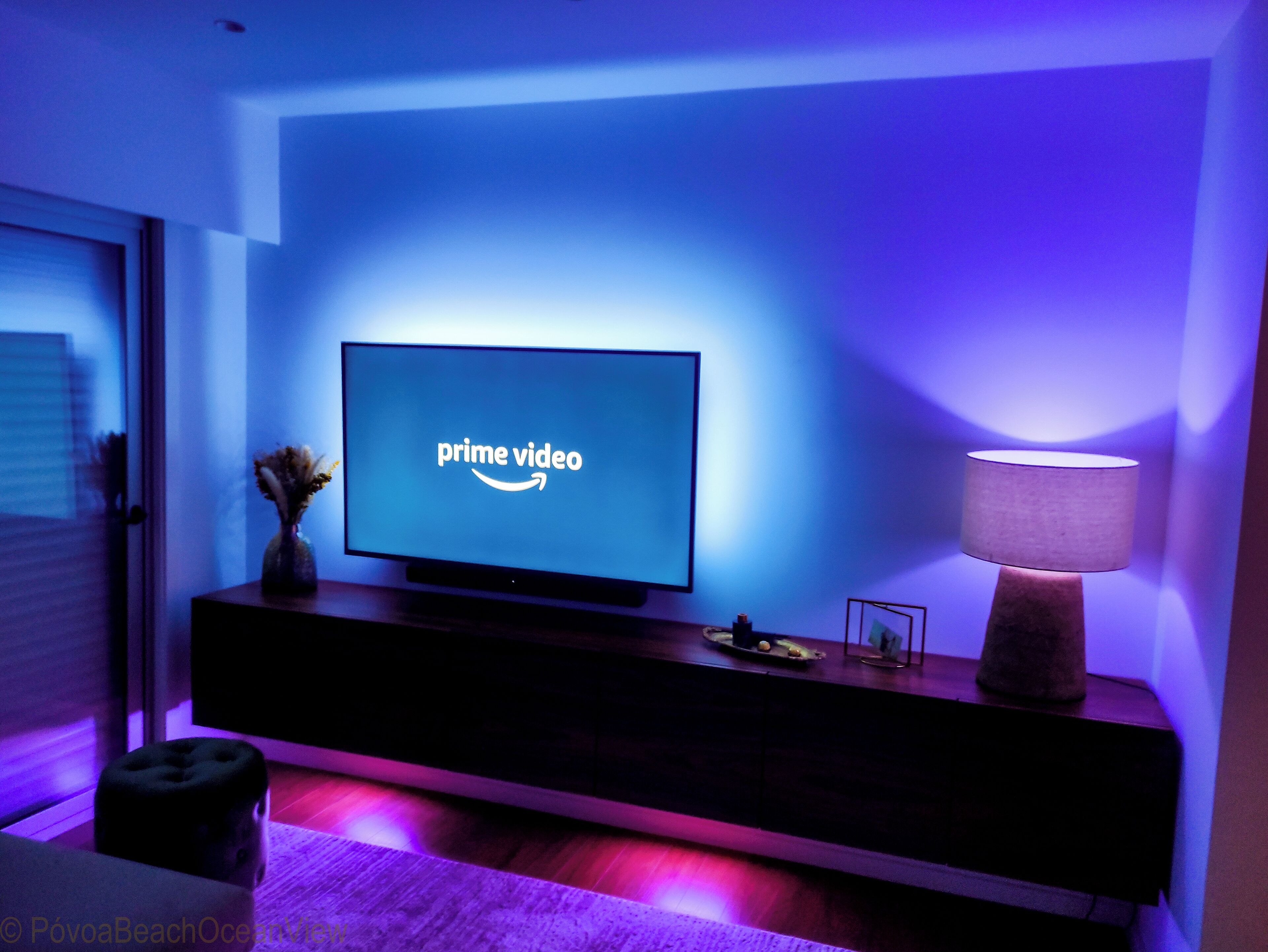 Un salon moderne doté d’un téléviseur à écran plat affichant le logo de Prime Video, d’un meuble de rangement en bois foncé et d’une lampe de table.