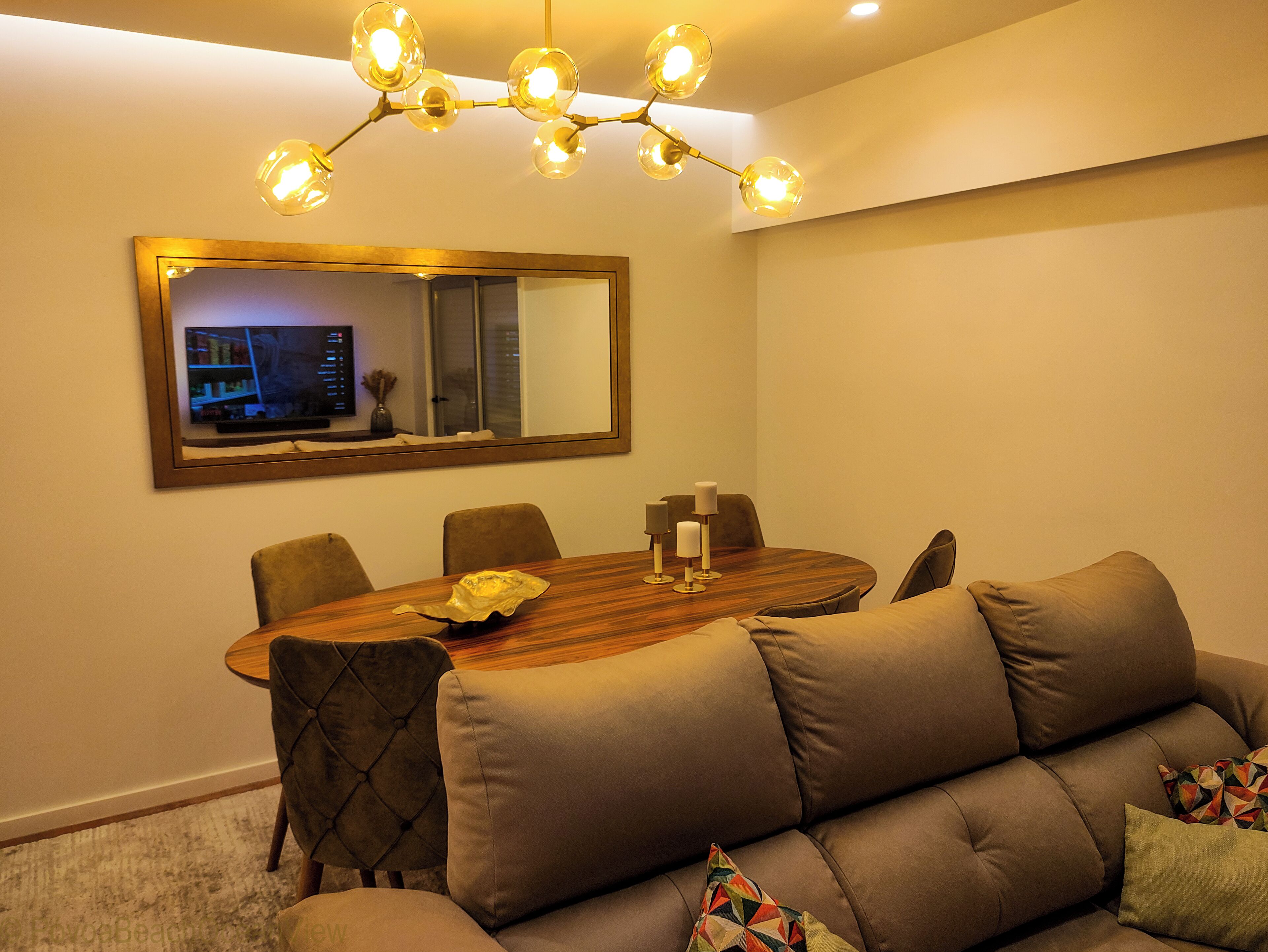 A modern dining area with a wooden table, six chairs, a sofa, and a large mirror above the table.