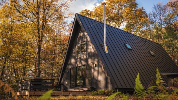 A modern, dark-colored cabin with a large window and a chimney, surrounded by autumn foliage. - Ridgeview A-Frame: Stylish Kerhonkson Escape (Kerhonkson)