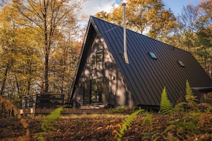 A modern, dark-colored cabin with a large window and a chimney, surrounded by autumn foliage. - Ridgeview A-Frame: Stylish Kerhonkson Escape (Kerhonkson)