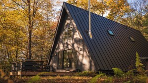 A modern, dark-colored cabin with a sloped roof, large windows, and a wooden deck. - Ridgeview A-Frame: Stylish Kerhonkson Escape (Kerhonkson)