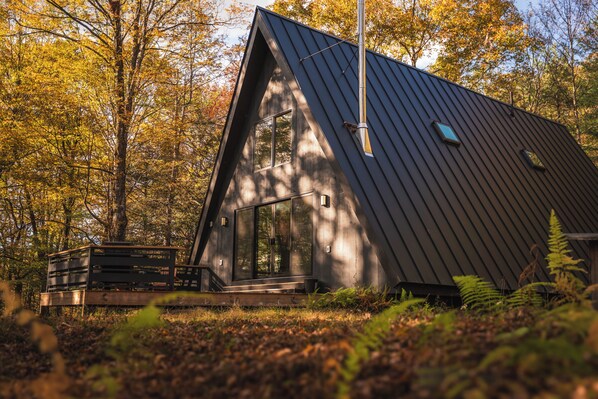 A modern, dark-colored cabin with a sloped roof, large windows, and a wooden deck. - Ridgeview A-Frame: Stylish Kerhonkson Escape (Kerhonkson)