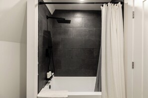 A modern bathroom with a dark tiled shower wall, a white bathtub, and a white shower curtain. - Ridgeview A-Frame: Stylish Kerhonkson Escape (Kerhonkson)
