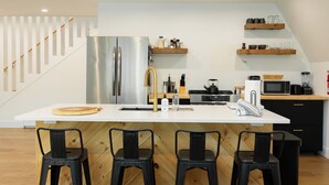 A modern kitchen with a stainless steel refrigerator, wooden bar stools, and built-in shelves. - Ridgeview A-Frame: Stylish Kerhonkson Escape (Kerhonkson)