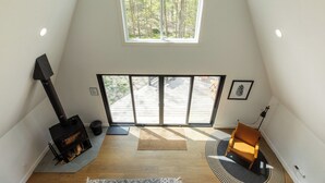 A high-ceilinged room with a large skylight, a fireplace, a sliding glass door to an outdoor deck, and a cozy seating area. - Ridgeview A-Frame: Stylish Kerhonkson Escape (Kerhonkson)