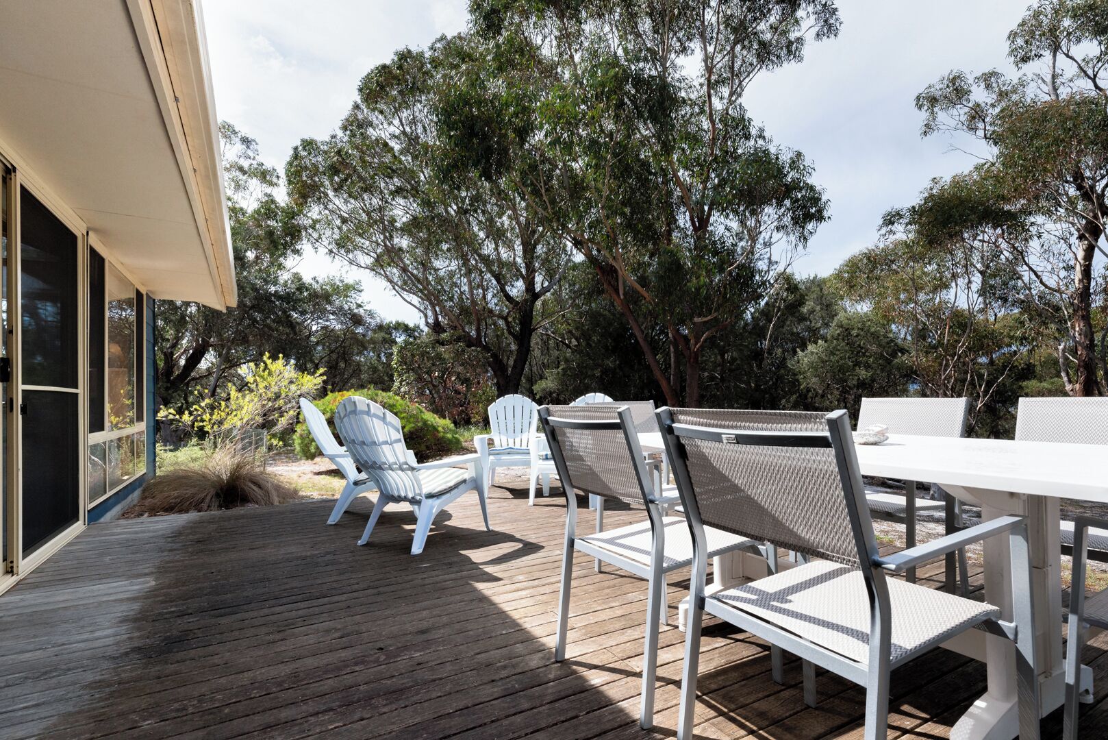 An outdoor deck with wooden flooring, white chairs, and a table.