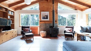 Ein gemütliches Wohnzimmer mit Kamin, Holzbalken, großen Fenstern und einem Fernseher.