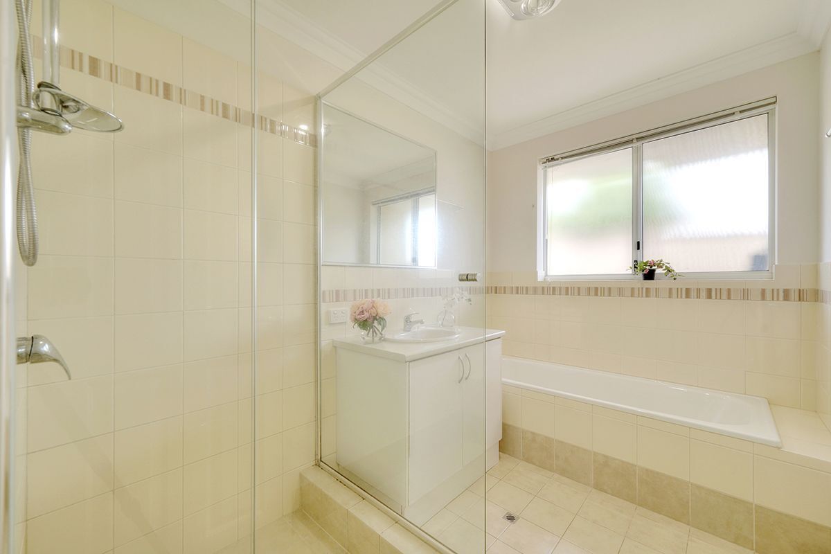 Ein modernes Badezimmer mit Duschkabine aus Glas, großem Spiegel, Badewanne und Fenster für natürliches Licht.