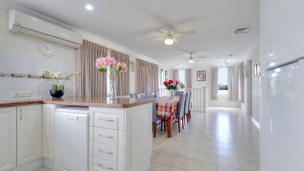 A modern kitchen with white cabinetry, a built-in dishwasher, a dining area with a table set for four, and a view of the city through large windows.