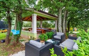 Eine Terrasse im Freien mit Tisch und Stühlen, umgeben von Grünpflanzen und Bäumen.