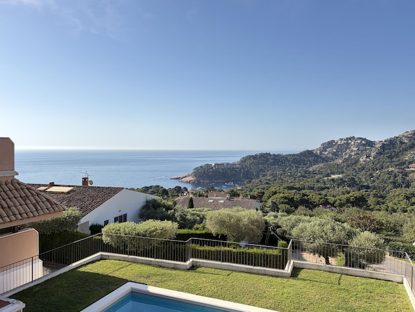 A residential property with a swimming pool, a view of the sea, and a hilly landscape.