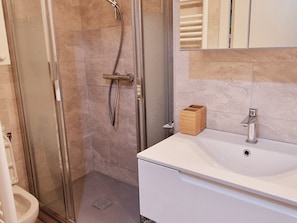Un baño con ducha de vidrio, un lavabo blanco y un espejo sobre el lavabo.