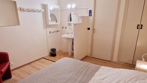Ein kleiner, sauberer Raum mit Bett, einem roten Sessel, einem weißen Waschbecken und einem Kleiderschrank.
