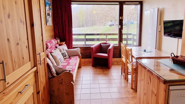 Ein gemütliches Zimmer mit einer Holzdirekt, einem roten Sessel, einem Esstisch und einem Fernseher.