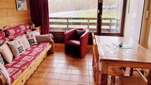 Ein gemütliches Zimmer mit einer Holzcouch, einem roten Sessel und einem Tisch.