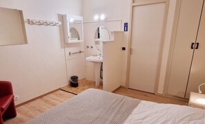 Habitación de hotel con cama, mesita de noche, espejo, lavamanos y armario.