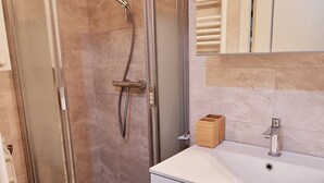 Ein Badezimmer mit einer Duschkabine, einem weißen Waschbecken und einem Spiegel darüber.