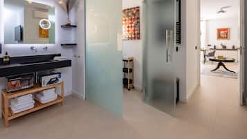 A modern bathroom with a large mirror, black countertop, and a wooden shelf with towels.