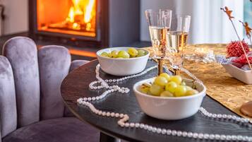 A round table with two bowls of green grapes, a string of pearls, and two glasses of a clear liquid, possibly wine, on a tablecloth with a gold pattern.