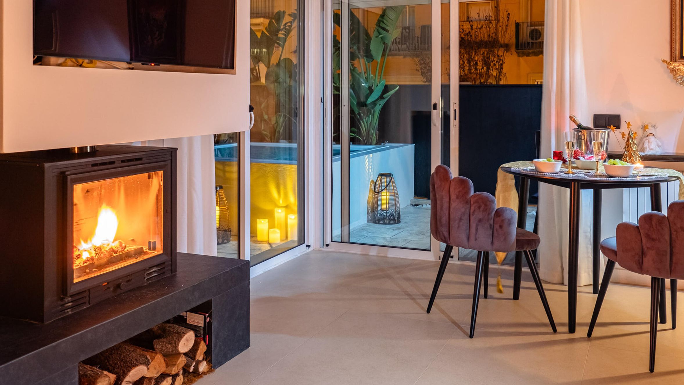 A modern living room with a fireplace, a dining area with chairs, and a view through glass doors to an outdoor space.