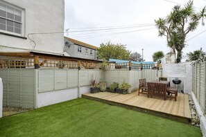 Un patio trasero con terraza de madera, una parrilla y plantas en macetas.