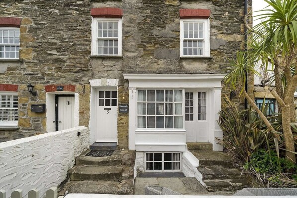 Un edificio de piedra con una puerta blanca que dice '7 Door Park', una ventana con cortina y un pequeño porche.