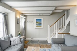 Una sala de estar con un sofá, una mesa de centro, una escalera y un cuadro en la pared.