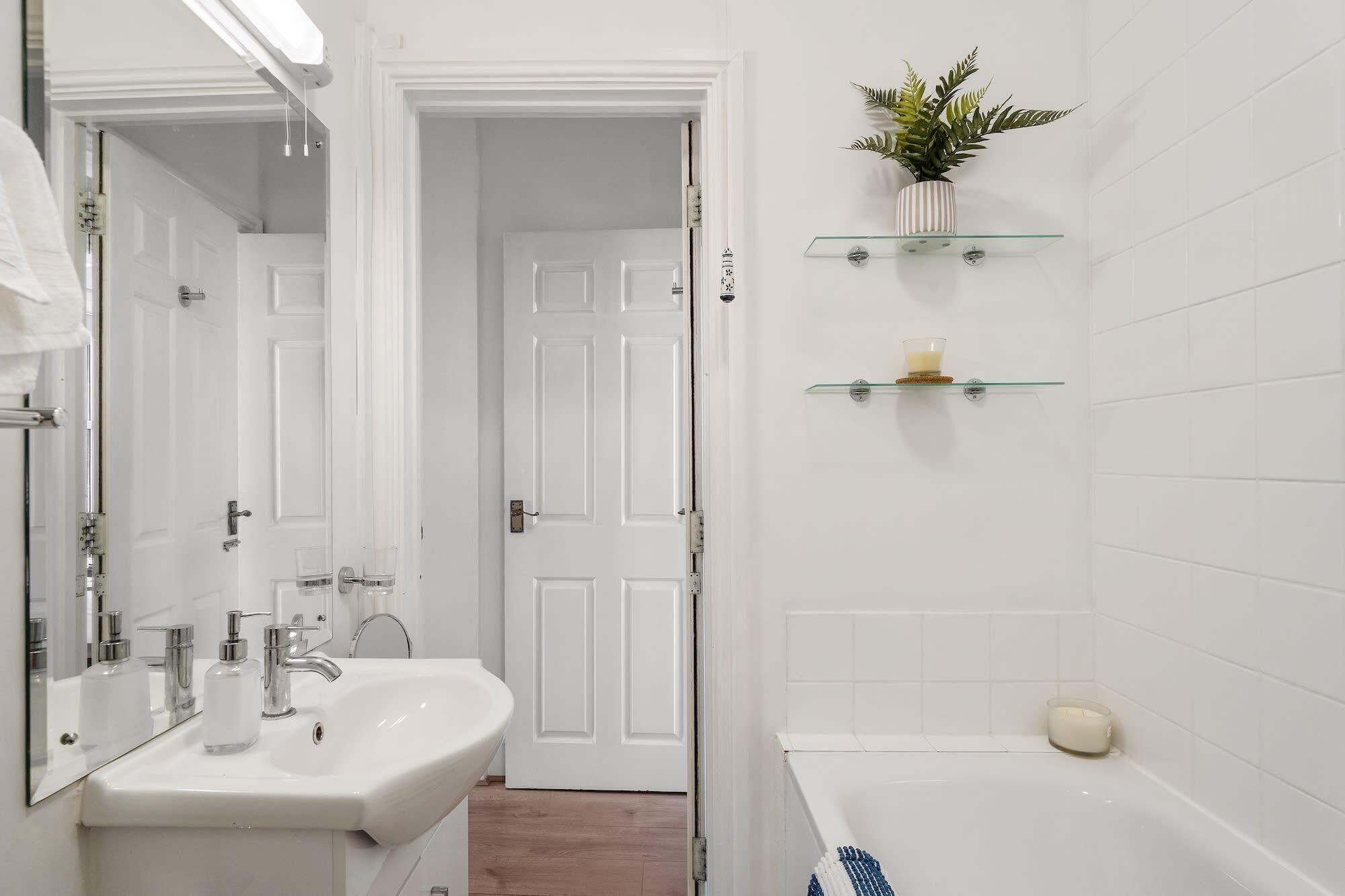 Un baño con lavamanos blanco, espejo y repisas de vidrio con artículos de aseo.