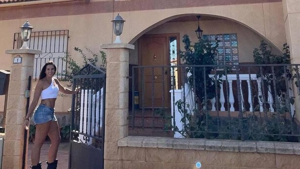 Une maison à deux étages avec un balcon, une entrée fermée par un portail et un ciel dégagé.