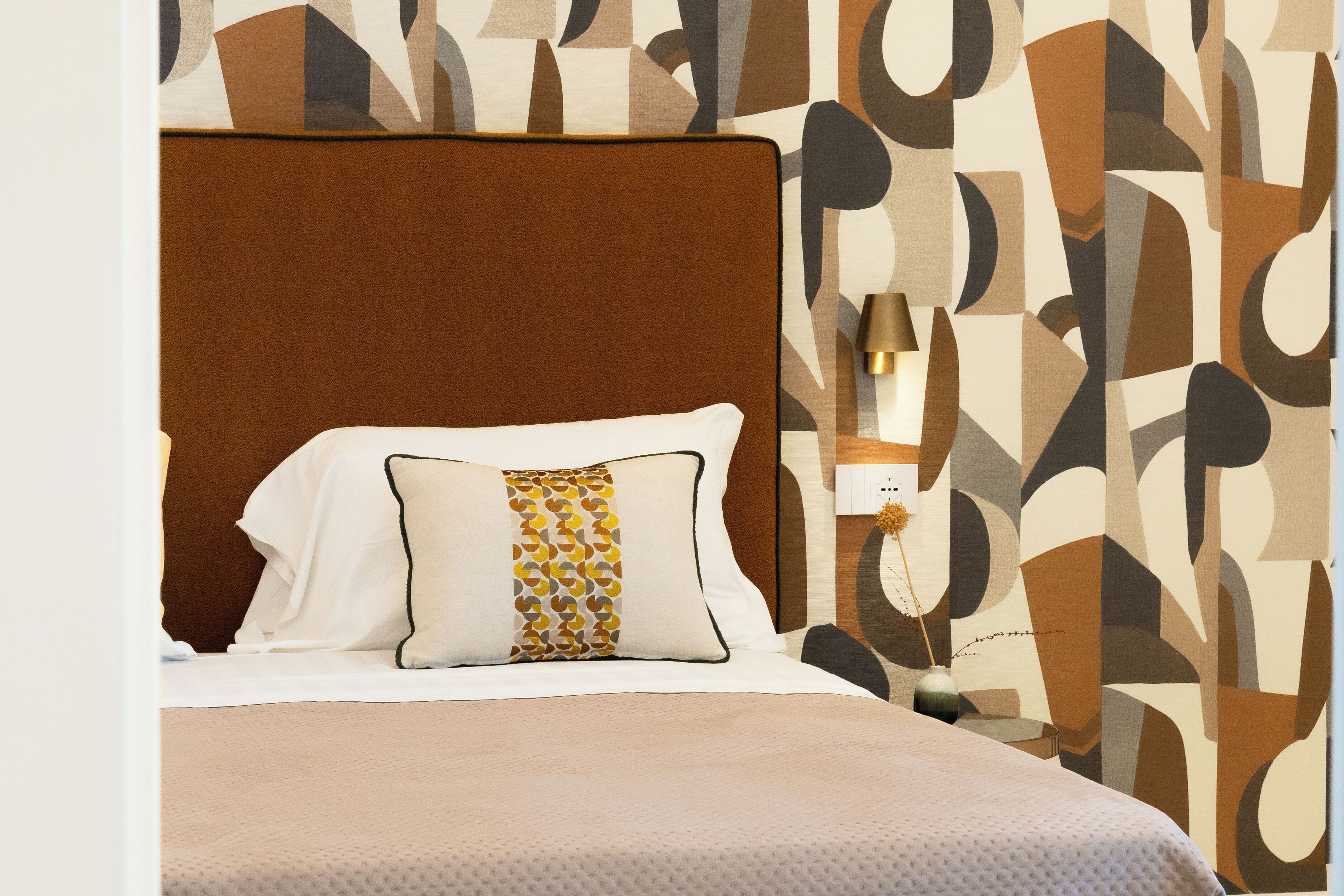 Un lit bien fait, avec une tête de lit marron, un oreiller blanc orné d’un motif géométrique et une couvre-lit beige.