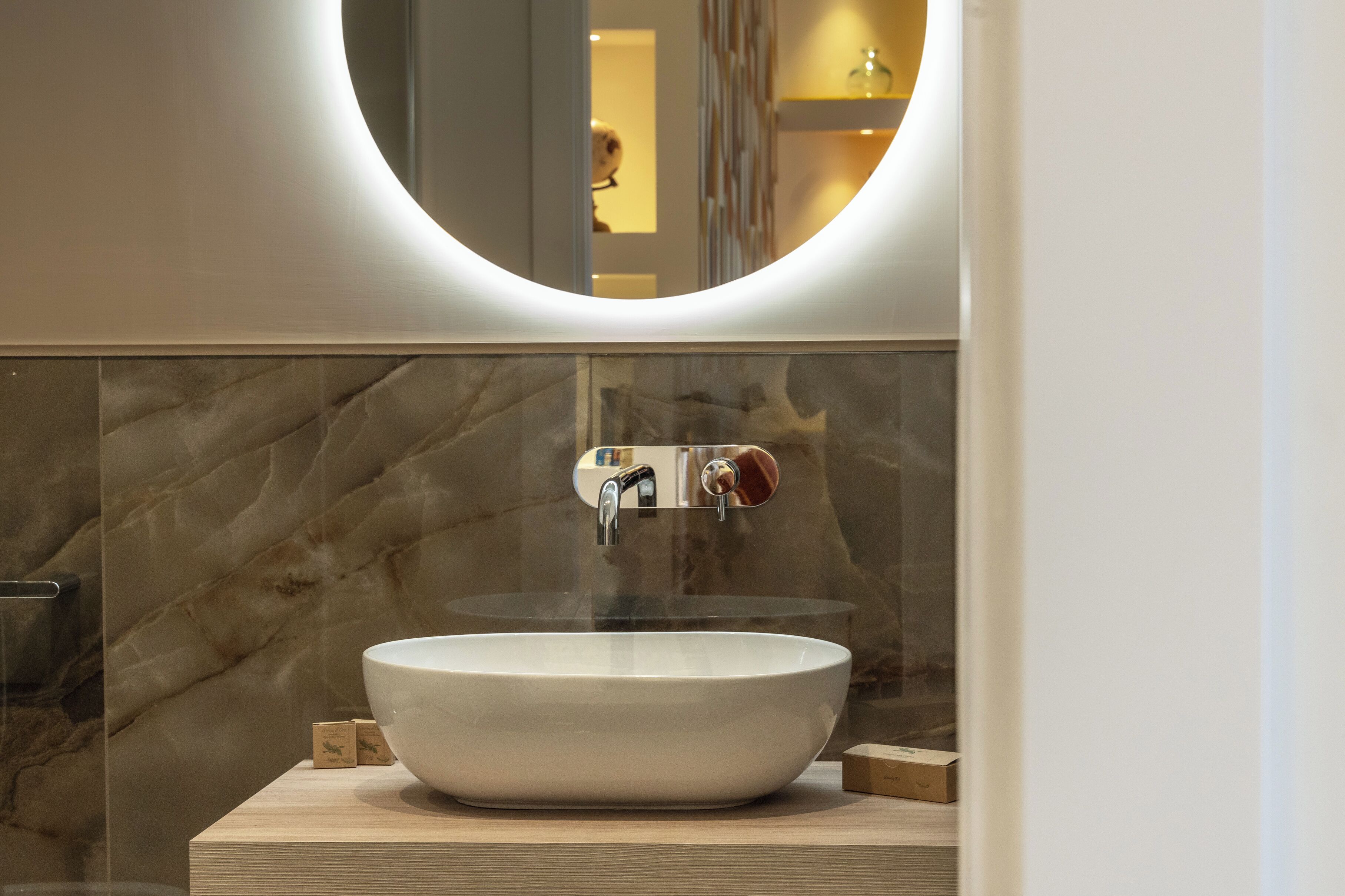Un baño moderno con un lavabo ovalado grande, un espejo encima y paredes de mármol.
