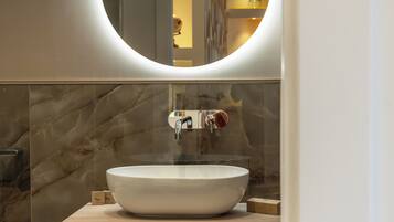 Un baño moderno con un lavabo ovalado grande, un espejo encima y paredes de mármol.